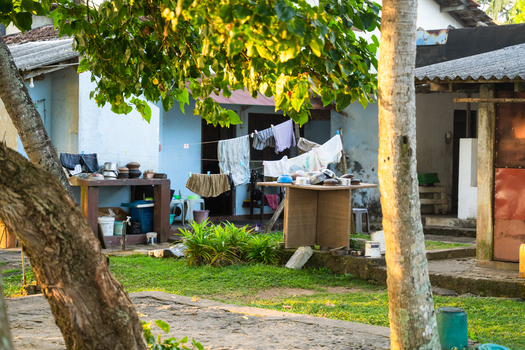 View of a traditional courtyard with laundry hanging on a line and kitchenware on a table under the shade of lush green trees in Galle Southern Province Sri Lanka.