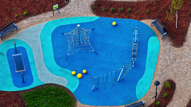 Aerial view of a colorful playground with a climbing net climbing frame and yellow balls on a blue and turquoise surface surrounded by wood chip mulch in Latvija. Aerial view of a colorful playground with a climbing net climbing frame and yellow balls on a blue and turquoise surface surrounded by wood chip mulch in Latvija.