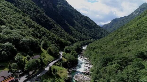 Aerial view of a river flowing through a lush mountain valley with a road and houses along the bank. Verzasca valley Switzerland Aerial view of a river flowing through a lush mountain valley with a road and houses along the bank. Verzasca valley Switzerland