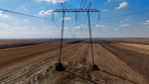 Aerial view of electric power transmission lines stretching across vast agricultural fields under a blue sky with scattered clouds in Pancevo Serbia.