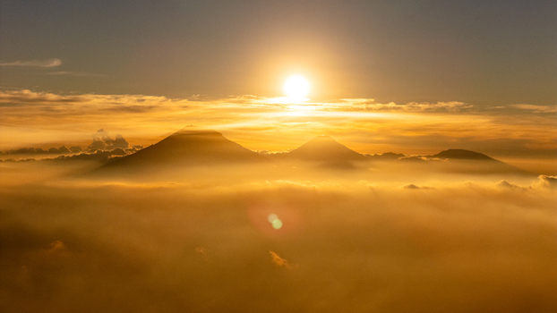 Aerial view of the volcanic peaks of Mount Sumbing and Mount Sindoro rising above a dense sea of clouds during a golden sunset in Selo Central Java Indonesia. Aerial view of the volcanic peaks of Mount Sumbing and Mount Sindoro rising above a dense sea of clouds during a golden sunset in Selo Central Java Indonesia.