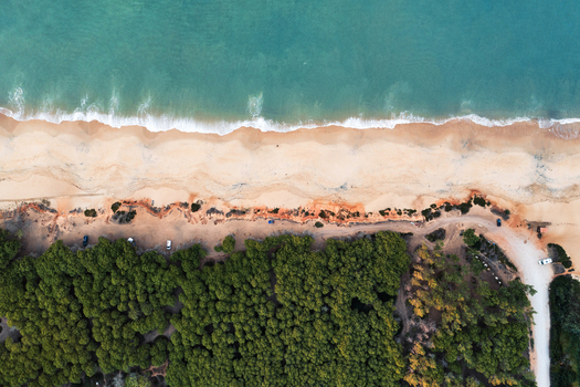 Aerial view of the sandy coastline of Faro with turquoise ocean waves a dense pine forest and a dirt road bordering the beach in Faro Faro District Portugal.