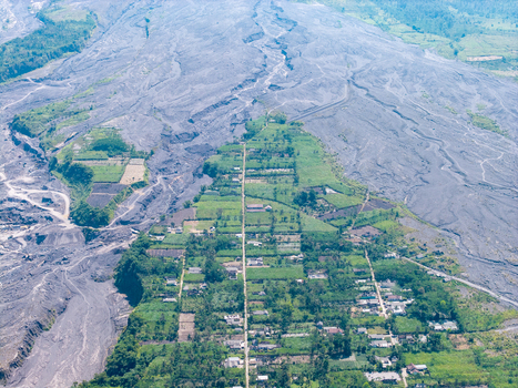 Aerial view of Supiturang Village showing the aftermath of the Mount Semeru eruption with volcanic ash deposits surrounding green fields and houses in Pronojiwo East Java Indonesia.
