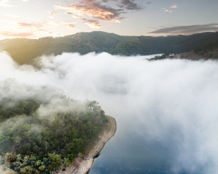 Aerial view of Kangaroo Creek Reservoir with thick fog rolling over the water and forested hills under a golden sunrise Adelaide Hills Council South Australia Australia. Aerial view of Kangaroo Creek Reservoir with thick fog rolling over the water and forested hills under a golden sunrise Adelaide Hills Council South Australia Australia.