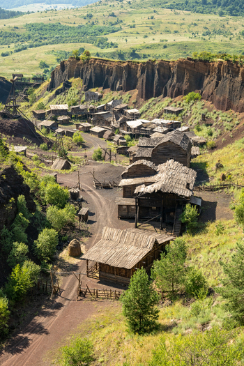 View of a rustic wooden village nestled in a valley surrounded by steep dark rocky cliffs and lush green hills in Brasov Brasov Romania.