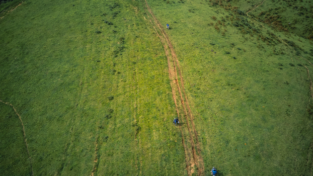 Aerial view of winding earthy paths cutting through vibrant undulating green hills with small figures traversing the natural terrain Obudu Cross River Nigeria.