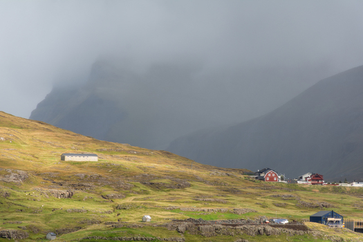 View of houses nestled on a green hillside with rocky terrain and a mountain shrouded in fog in the Faroe Islands.