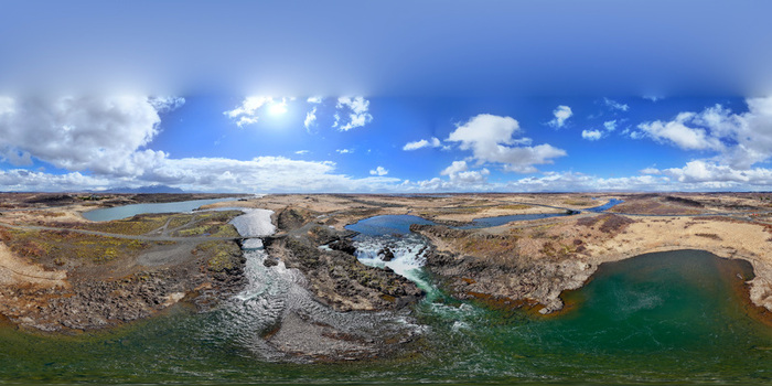 Aerial view of the Glanni waterfall and Nordura river flowing through a rugged volcanic landscape under a bright blue sky with scattered clouds in Borgarbyggd Iceland.