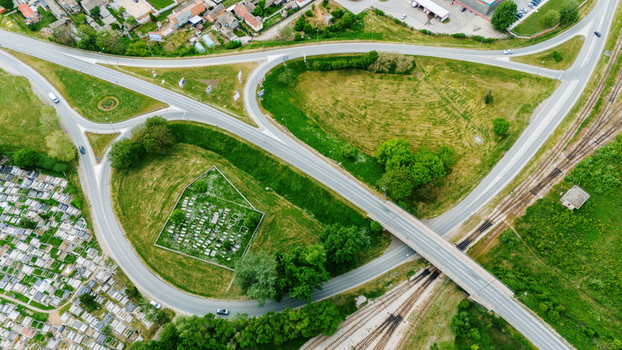 Aerial view of a complex road interchange with a small cemetery and railway tracks surrounded by green fields and urban buildings in Sabac Vojvodina Serbia.