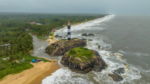 Aerial view of Kapu Light House situated on a rocky outcrop surrounded by the Arabian Sea with lush palm trees and crashing waves along the coastline in Udupi Karnataka India.