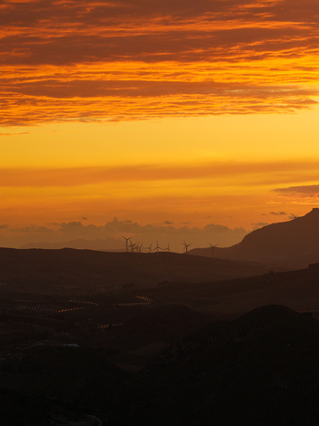 Aerial view of wind turbines silhouetted against a vibrant orange sunset over the hills of Riserva Naturale Orientata dello Zingaro San Vito Lo Capo Sicilia Italy. Aerial view of wind turbines silhouetted against a vibrant orange sunset over the hills of Riserva Naturale Orientata dello Zingaro San Vito Lo Capo Sicilia Italy.