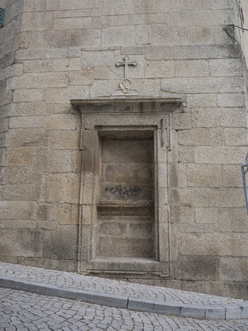 View of a historic stone niche with a carved cross set into a granite wall on a cobblestone street in Covilha Castelo Branco District Portugal.