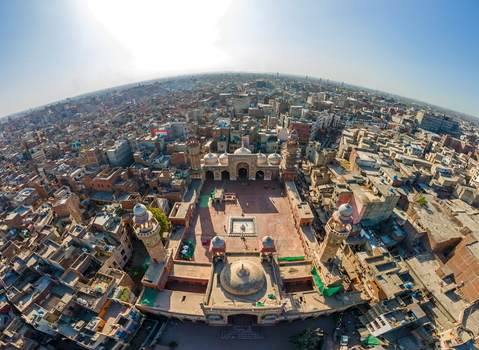 Aerial view of Wazir Khan Mosque a historic 17th century mosque with intricate tile work and minarets surrounded by the dense urban rooftops of the old city in Lahore Punjab Pakistan.