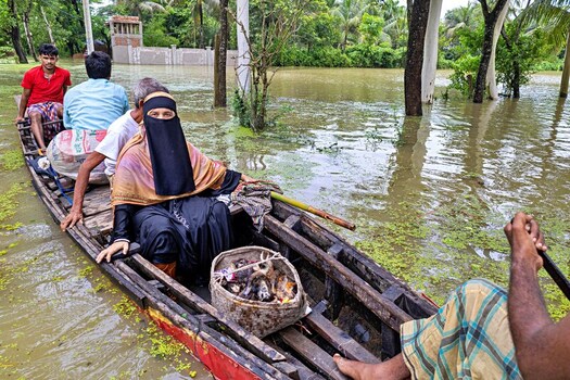 Banshkhali Upazila Chittagong Division Bangladesh 10 July 2026 View of people navigating a flooded area in a wooden boat carrying belongings through submerged landscape. Banshkhali Upazila Chittagong Division Bangladesh 10 July 2026 View of people navigating a flooded area in a wooden boat carrying belongings through submerged landscape.