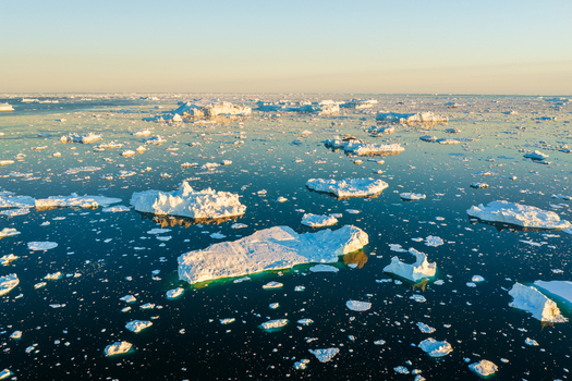 Aerial view of icebergs floating in the dark blue waters of the Ilulissat Icefjord under a clear sky in Ilulissat Avannaata Greenland.