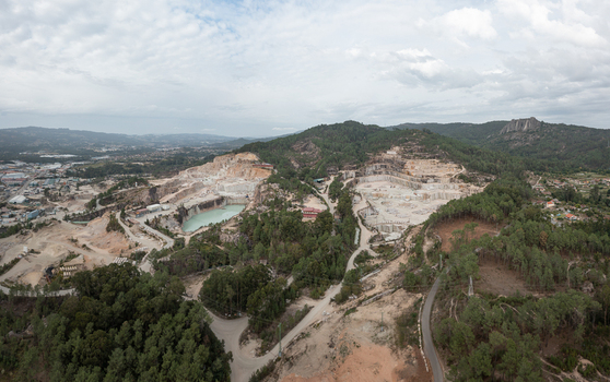 Aerial view of Cantera Porrino showing open pit granite mining operations with a turquoise water pool surrounding pine forests and industrial roads in O Porrino Pontevedra Spain. Aerial view of Cantera Porrino showing open pit granite mining operations with a turquoise water pool surrounding pine forests and industrial roads in O Porrino Pontevedra Spain.