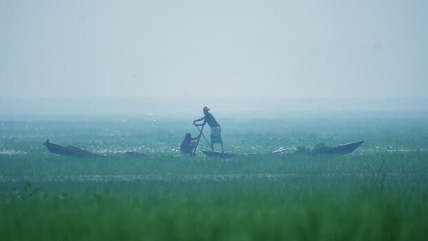 View of a fisherman in a boat on a misty river in Bangladesh.