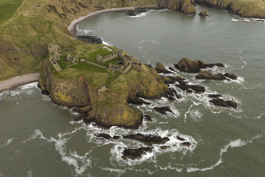 Aerial view of the medieval ruins of Dunnottar Castle perched on a rocky headland surrounded by the North Sea and green coastal cliffs in Stonehaven Scotland United Kingdom. Aerial view of the medieval ruins of Dunnottar Castle perched on a rocky headland surrounded by the North Sea and green coastal cliffs in Stonehaven Scotland United Kingdom.