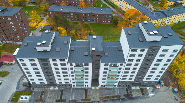Aerial view of a modern apartment building with a dark roof and white facade surrounded by autumn trees and a parking area in Sweden. Aerial view of a modern apartment building with a dark roof and white facade surrounded by autumn trees and a parking area in Sweden.