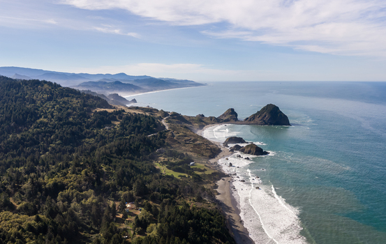 Aerial view of the rugged Southern Oregon Coast featuring dramatic sea stacks forested cliffs and crashing waves along the Pacific Ocean shoreline in Port Orford Oregon United States. Aerial view of the rugged Southern Oregon Coast featuring dramatic sea stacks forested cliffs and crashing waves along the Pacific Ocean shoreline in Port Orford Oregon United States.