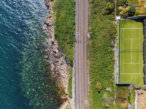 Aerial view of the Dalkey coastline featuring a railway track running alongside the sea and a tennis court situated on the cliffside in Dublin County Dublin Ireland. Aerial view of the Dalkey coastline featuring a railway track running alongside the sea and a tennis court situated on the cliffside in Dublin County Dublin Ireland.
