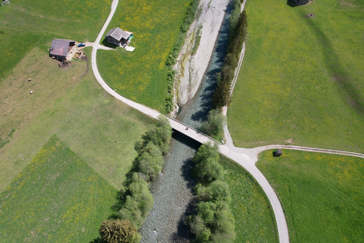 Aerial view of a river flowing under a small bridge surrounded by green meadows and rustic barns in Rougemont Vaud Switzerland. Aerial view of a river flowing under a small bridge surrounded by green meadows and rustic barns in Rougemont Vaud Switzerland.