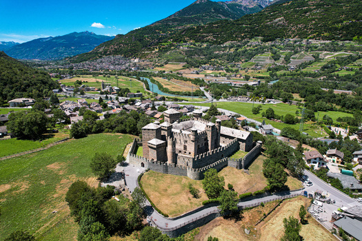 Aerial view of the medieval Fenis Castle with its stone towers and crenellated walls surrounded by green fields and alpine mountains in Fenis Aosta Valley Italy. Aerial view of the medieval Fenis Castle with its stone towers and crenellated walls surrounded by green fields and alpine mountains in Fenis Aosta Valley Italy.