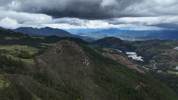 Aerial view of the mountainous landscape near Carretera al Salto de Aguas Blancas with green hills agricultural greenhouses and a cloudy sky in Constanza La Vega Dominican Republic.