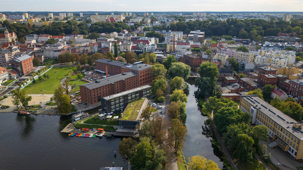 Aerial view of the contrasting textures of red brick buildings and the serene canal reflecting the sky surrounded by lush greenery Bydgoszcz Województwo kujawsko pomorskie Poland. Aerial view of the contrasting textures of red brick buildings and the serene canal reflecting the sky surrounded by lush greenery Bydgoszcz Województwo kujawsko pomorskie Poland.