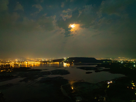Aerial view of the illuminated cityscape of Udaipur at night with city lights reflecting on the calm waters of Lake Pichola under a cloudy sky in Udaipur Rajasthan India.