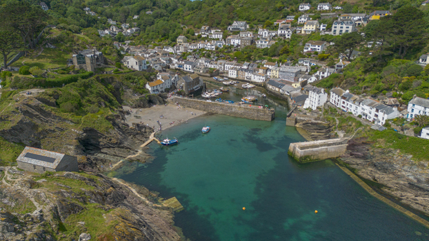 Aerial view of the historic coastal village of Polperro featuring stone cottages a sheltered harbor with fishing boats and turquoise waters in Polperro Cornwall United Kingdom. Aerial view of the historic coastal village of Polperro featuring stone cottages a sheltered harbor with fishing boats and turquoise waters in Polperro Cornwall United Kingdom.