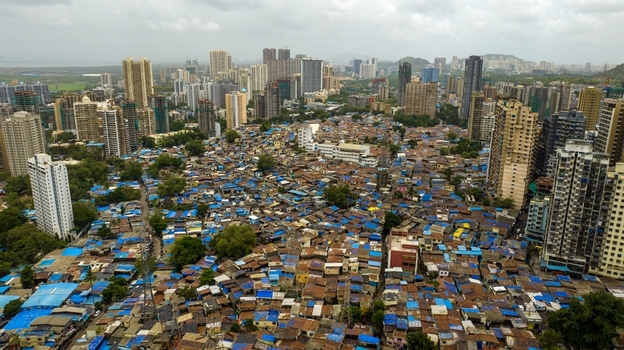Aerial view of Dharavi Slums featuring dense low rise housing with blue tarpaulin roofs contrasted against modern high rise skyscrapers in Mumbai Maharashtra India. Aerial view of Dharavi Slums featuring dense low rise housing with blue tarpaulin roofs contrasted against modern high rise skyscrapers in Mumbai Maharashtra India.
