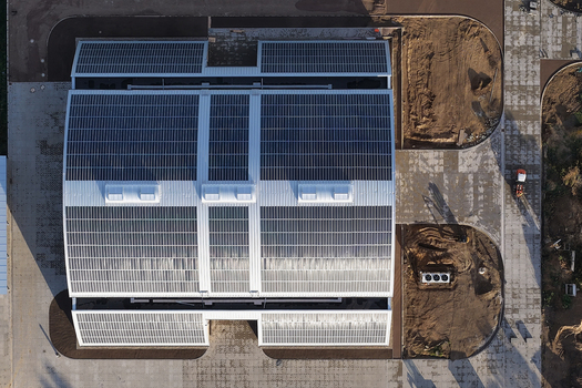 Aerial view of a large building with extensive solar panel arrays on its roof surrounded by construction areas and paved paths in Uckermark Brandenburg Germany. Aerial view of a large building with extensive solar panel arrays on its roof surrounded by construction areas and paved paths in Uckermark Brandenburg Germany.