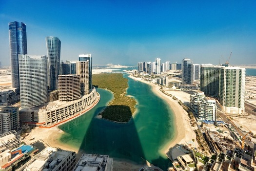 View of modern skyscrapers and high rise buildings surrounding a turquoise canal with a mangrove island under a clear blue sky in Abu Dhabi Abu Dhabi United Arab Emirates. View of modern skyscrapers and high rise buildings surrounding a turquoise canal with a mangrove island under a clear blue sky in Abu Dhabi Abu Dhabi United Arab Emirates.