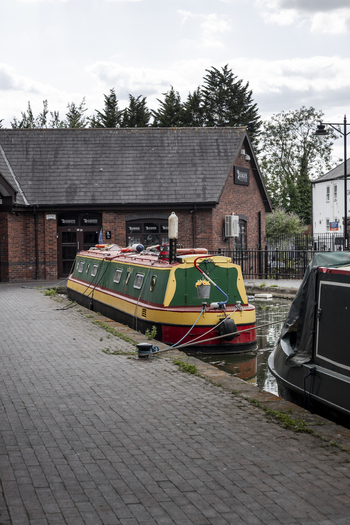 Coventry England United Kingdom 20 July 2026 View of a colorful narrowboat moored along a brick paved canal towpath next to a brick building under a cloudy sky.