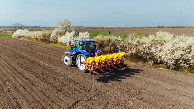 Aerial view of a blue tractor amidst freshly tilled fields with white blossoming trees lining the horizon casting long shadows Sremska Mitrovica Vojvodina Serbia. Aerial view of a blue tractor amidst freshly tilled fields with white blossoming trees lining the horizon casting long shadows Sremska Mitrovica Vojvodina Serbia.