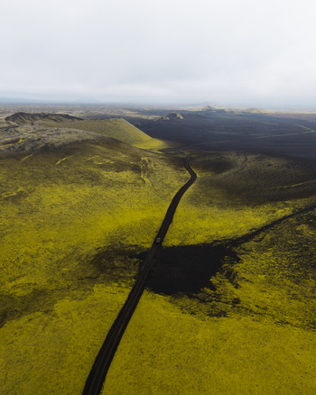 Aerial view of a stark road slicing through vibrant green moss fields against a backdrop of shadowy volcanic rock Lakagigar Iceland. Aerial view of a stark road slicing through vibrant green moss fields against a backdrop of shadowy volcanic rock Lakagigar Iceland.