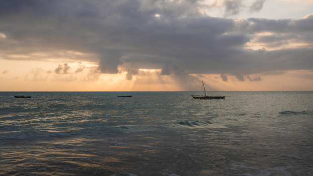 View of the tranquil turquoise waters reflecting the golden sunset with traditional boats silhouetted against the horizon under a dramatic sky Paje Tanzania. View of the tranquil turquoise waters reflecting the golden sunset with traditional boats silhouetted against the horizon under a dramatic sky Paje Tanzania.