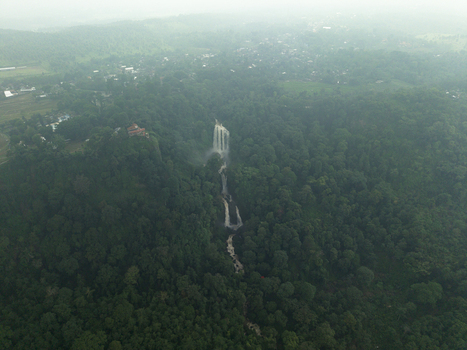 Aerial view of cascading waterfalls plunge through the dense verdant forest canopy a misty veil hanging in the air Curugsewu Kendal Regency Central Java Indonesia. Aerial view of cascading waterfalls plunge through the dense verdant forest canopy a misty veil hanging in the air Curugsewu Kendal Regency Central Java Indonesia.