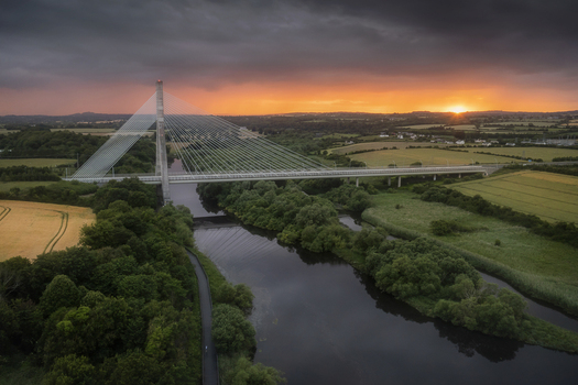 Aerial view of Mary McAleese Boyne Valley Bridge spanning the River Boyne amidst lush green fields and trees at sunset Drogheda County Louth Ireland. Aerial view of Mary McAleese Boyne Valley Bridge spanning the River Boyne amidst lush green fields and trees at sunset Drogheda County Louth Ireland.