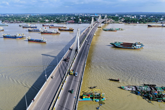 Aerial view of the Shah Amanat Bridge spanning the Karnaphuli River with cargo ships and small boats navigating the waterway in Chattogram Chittagong Division Bangladesh.