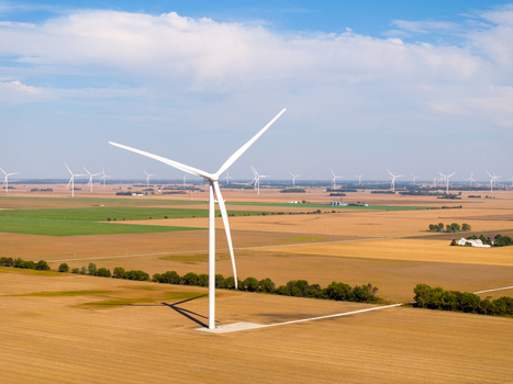 Aerial view of a wind turbine in a vast agricultural field with many other wind turbines across the landscape under a clear blue sky in Wolcott Indiana United States.