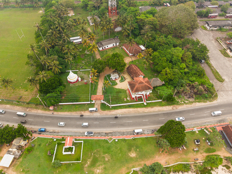 Aerial view of a Buddhist temple with a white stupa lush palm trees and vehicles driving along the coastal road in Koggala Southern Province Sri Lanka. Aerial view of a Buddhist temple with a white stupa lush palm trees and vehicles driving along the coastal road in Koggala Southern Province Sri Lanka.