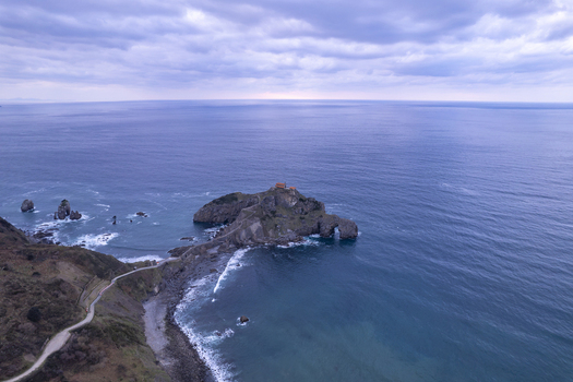 Aerial view of San Juan de Gaztelugatxe a historic hermitage on a rocky islet connected by a stone bridge to the rugged coastline in Gaztelugatxeko Doniene Euskadi Spain.