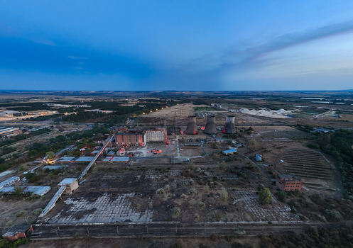 Aerial view of the closed Inota thermal power plant its cooling towers illuminated for a festival amid industrial grounds and surrounding fields at dusk in Hungary.