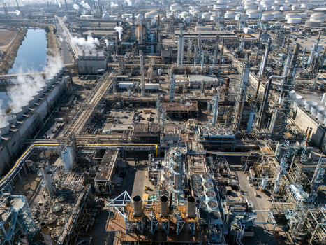 Aerial view of a large industrial oil refinery complex featuring intricate pipes storage tanks cooling towers and steam emissions in Carson California United States.