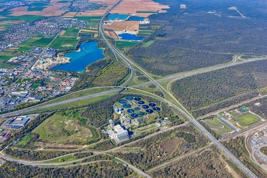 Aerial view of the intricate highway interchange weaving past the Sausheim water treatment plant a vibrant lake and dense forest Sausheim Grand Est France.