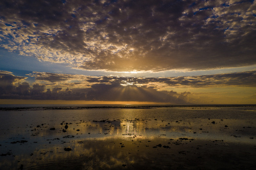 Aerial view of the sun setting over a calm lagoon with dramatic sun rays piercing through a cloudy sky and reflecting on the water surface Moka District Mauritius. Aerial view of the sun setting over a calm lagoon with dramatic sun rays piercing through a cloudy sky and reflecting on the water surface Moka District Mauritius.