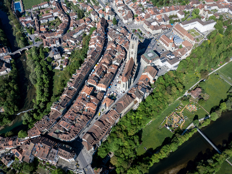 Aerial view of St Nicolas Cathedral surrounded by historic red tiled rooftops and lush green trees along the river in Fribourg Fribourg Switzerland. Aerial view of St Nicolas Cathedral surrounded by historic red tiled rooftops and lush green trees along the river in Fribourg Fribourg Switzerland.