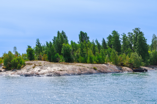 View of the rocky coastline with lush green trees and calm blue waters in Helsinki Uusimaa Finland.